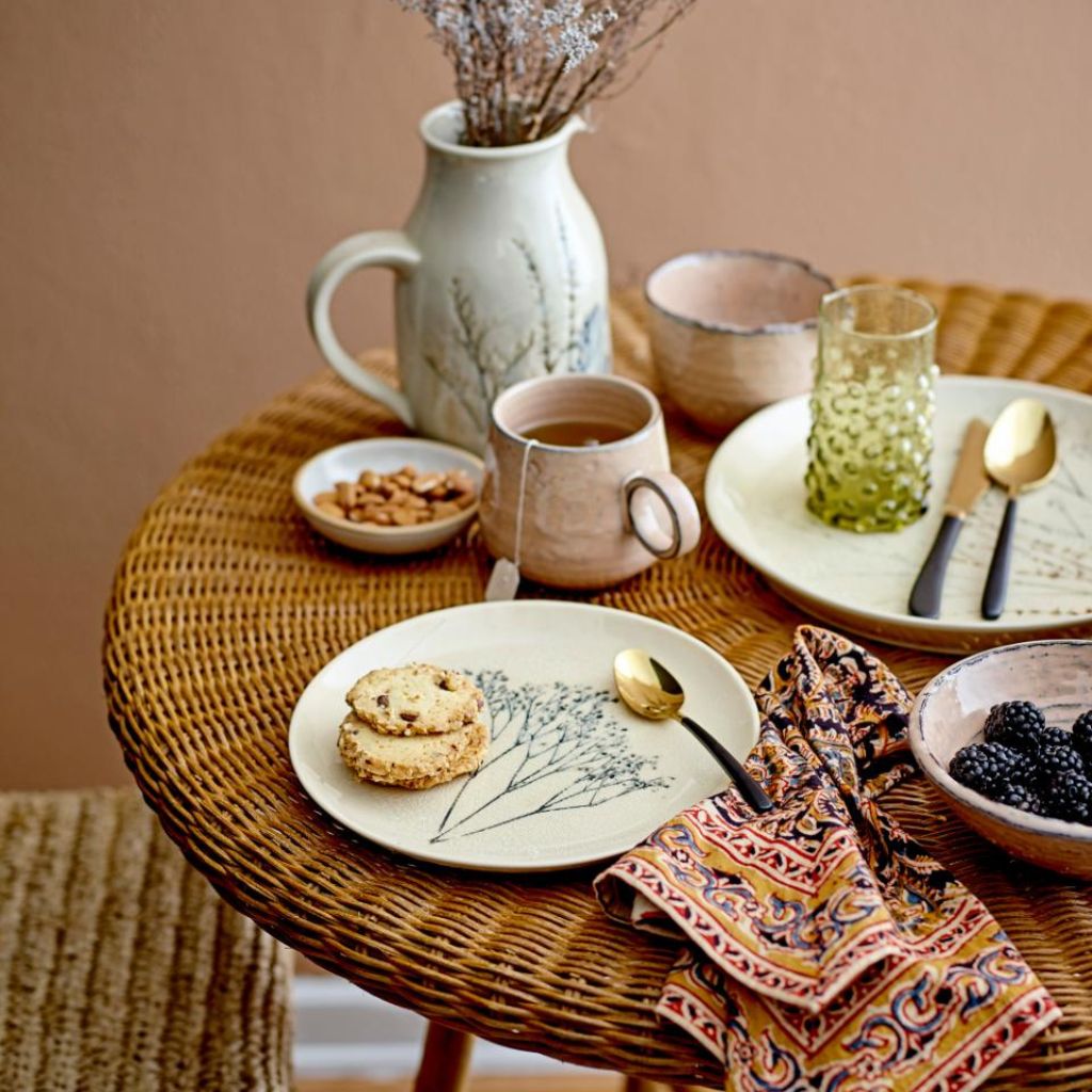 Table setting with a mug, cookies, and a vase on a woven table.