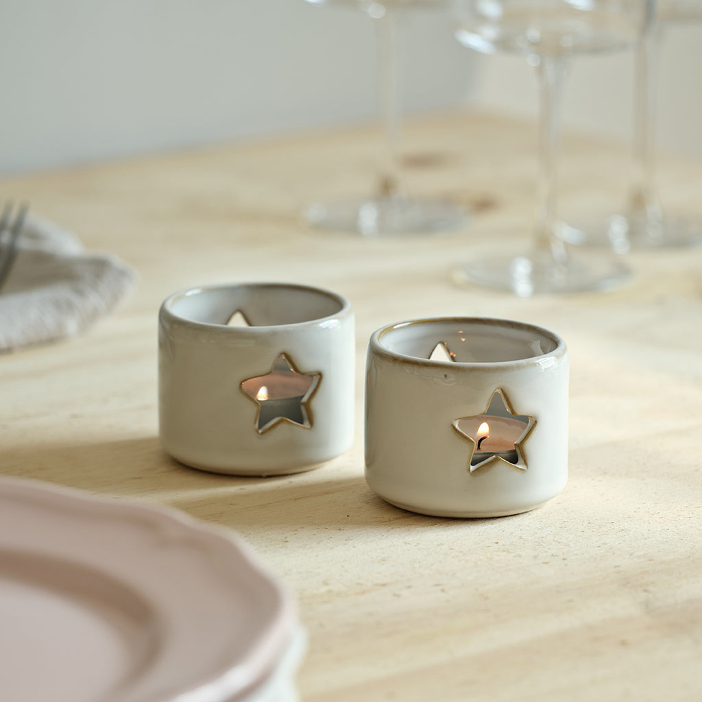 Two ceramic candle holders with star designs on a wooden table.