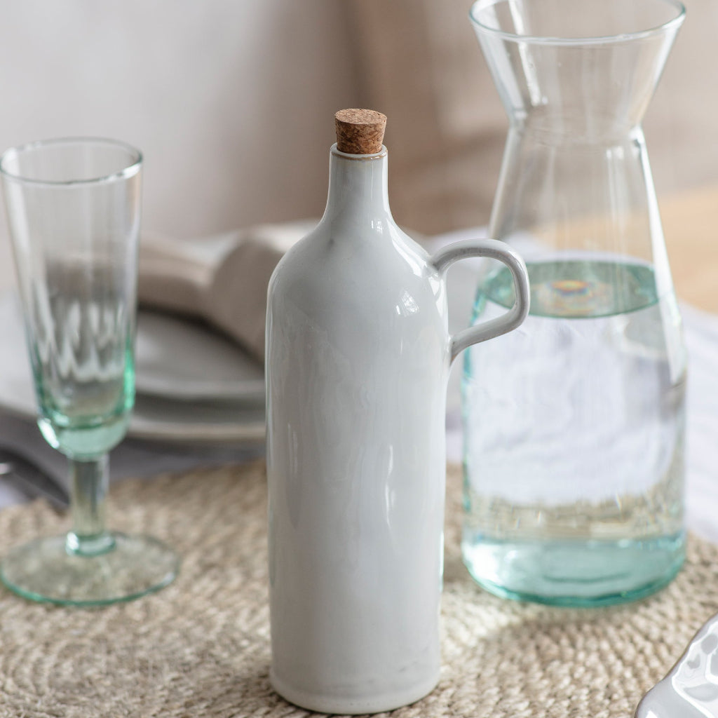 Decorative table setting with a white ceramic bottle, glass carafe, and glasses on a textured surface.