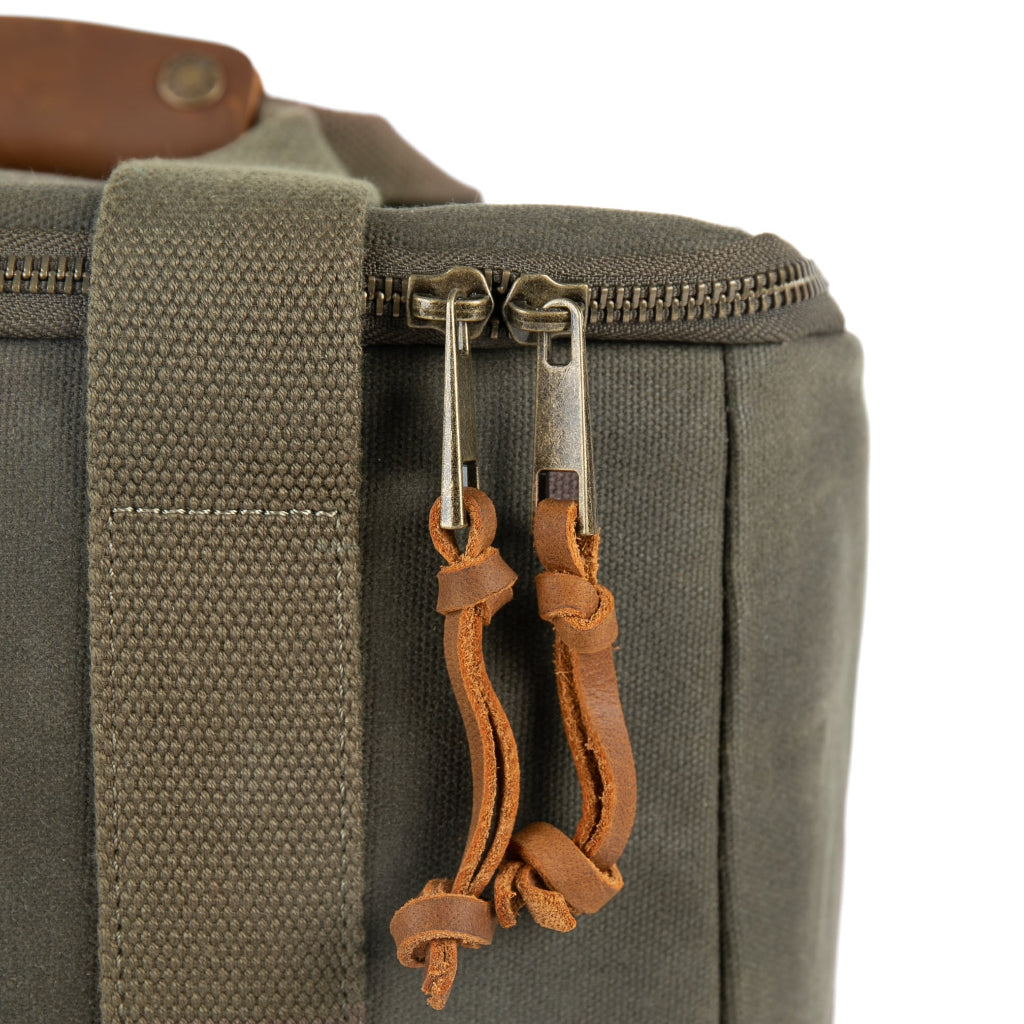 Close-up of a dark olive green canvas bag with dual metal zipper pulls wrapped in brown leather cords, on a white background.