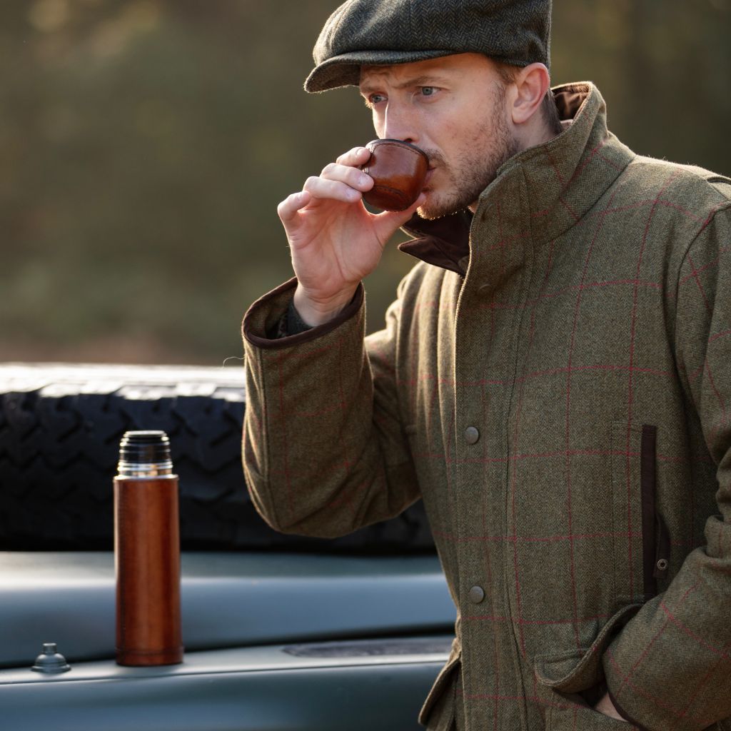 Person drinking from cup of leather cased thermos flask with thermos flask in background on landrover