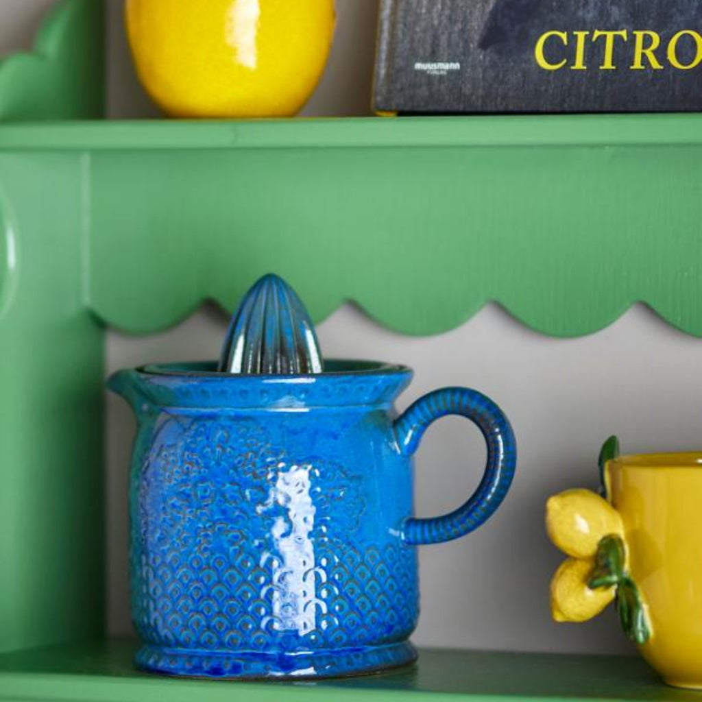 Blue lemon squeezer on a green shelf with decorative lemons and a book in the background.