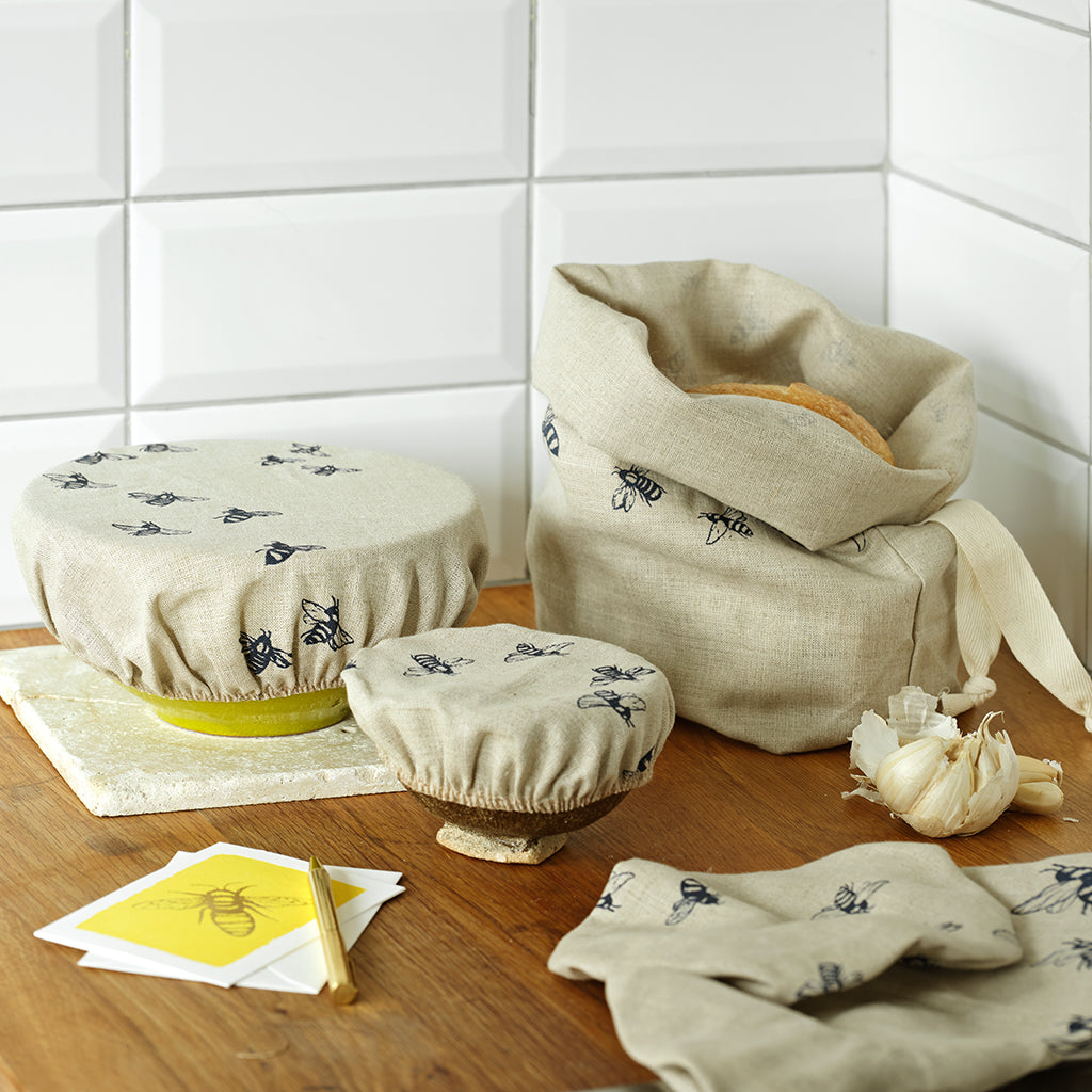 Set of fabric covers with bee pattern on a wooden surface against a white tiled wall.