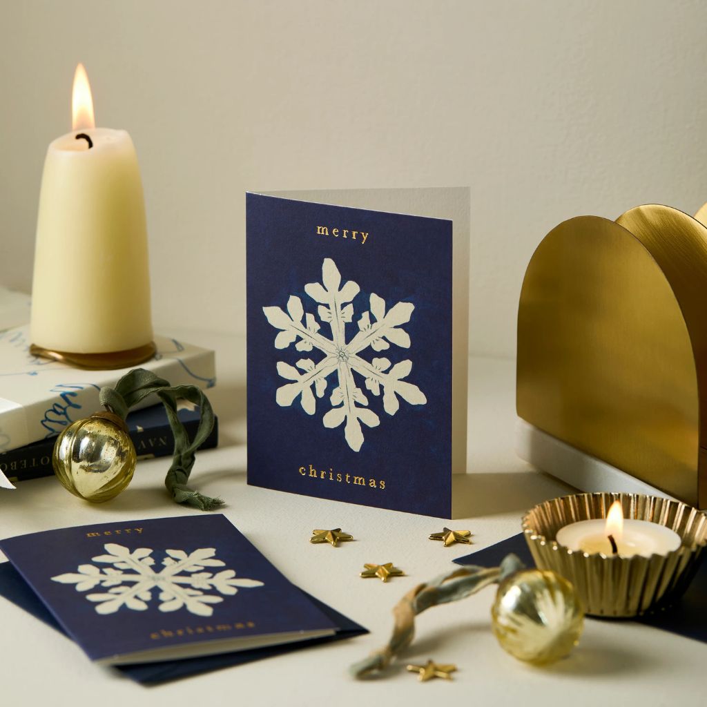 Navy blue Christmas card with white snowflake design on a table with candles and decorations.