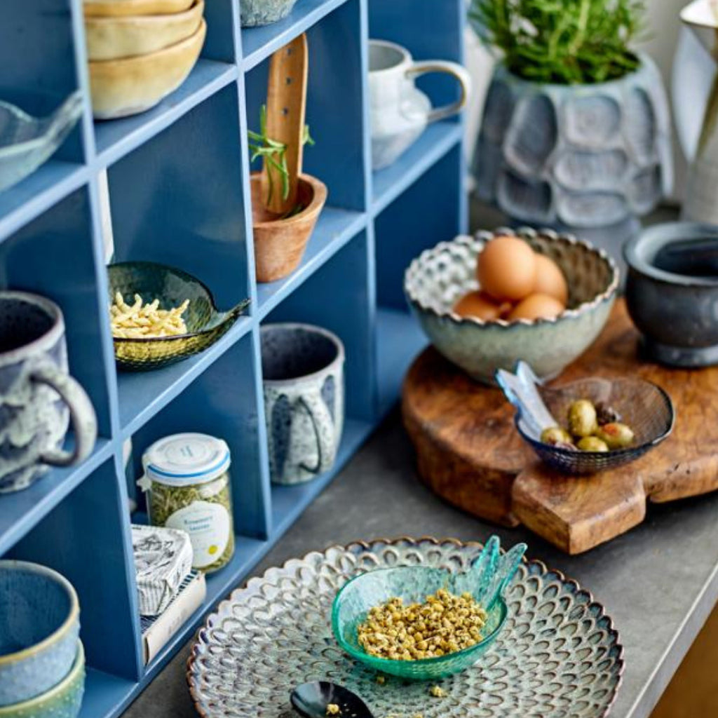 Kitchen scene with blue shelves, bowls, mugs, and a wooden cutting board.
