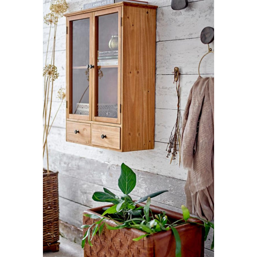 Wooden cabinet with glass doors on a wall with a plant and basket below.