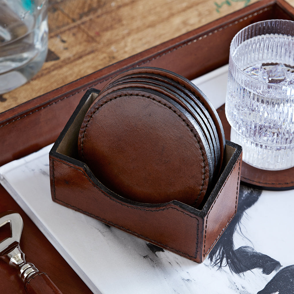 Set of round leaher coasters on leather tray with a bottle opener and glass of water on a single round coaster