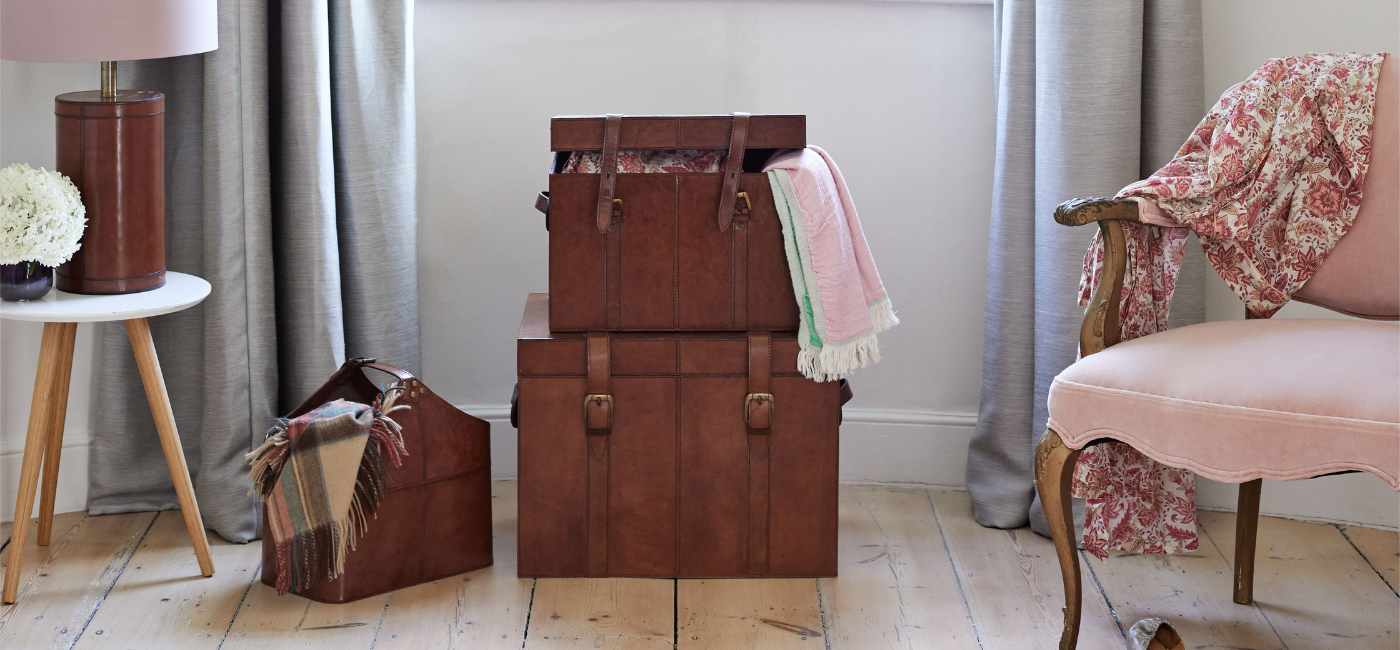 Set of two leather chests in bedroom setting with buckled magazine storage basket and leather lamp base on table