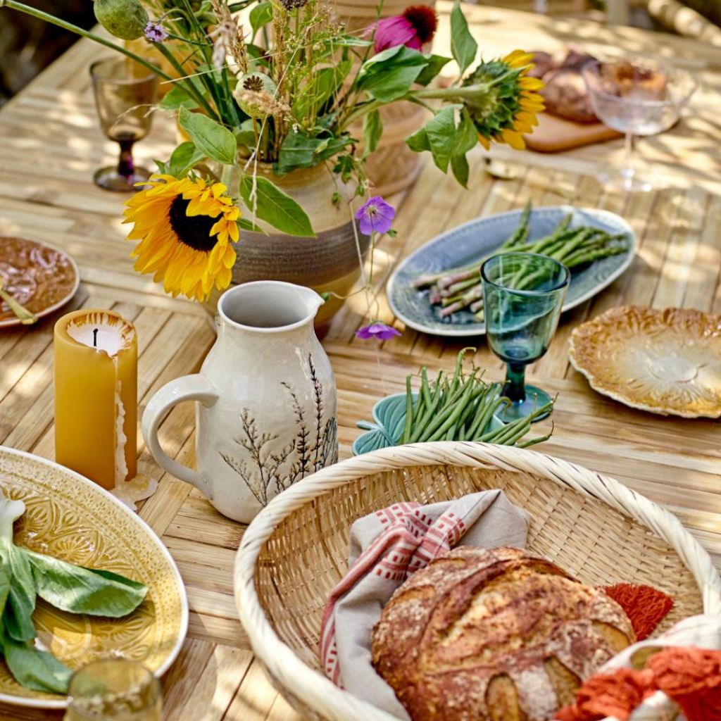 Outdoor dining table with bread, flowers, and plates on a wooden surface