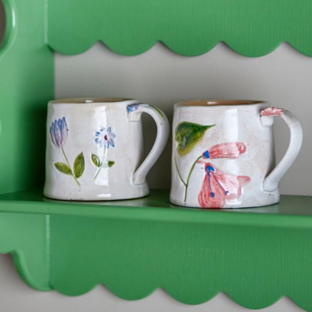 Two decorated mugs on a green shelf with a scalloped edge.