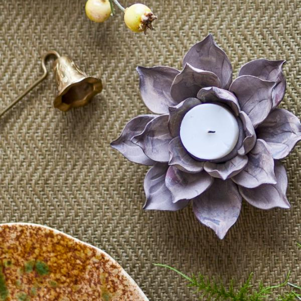 Decorative candle holder shaped like a flower on a textured surface with a ceramic dish and greenery.