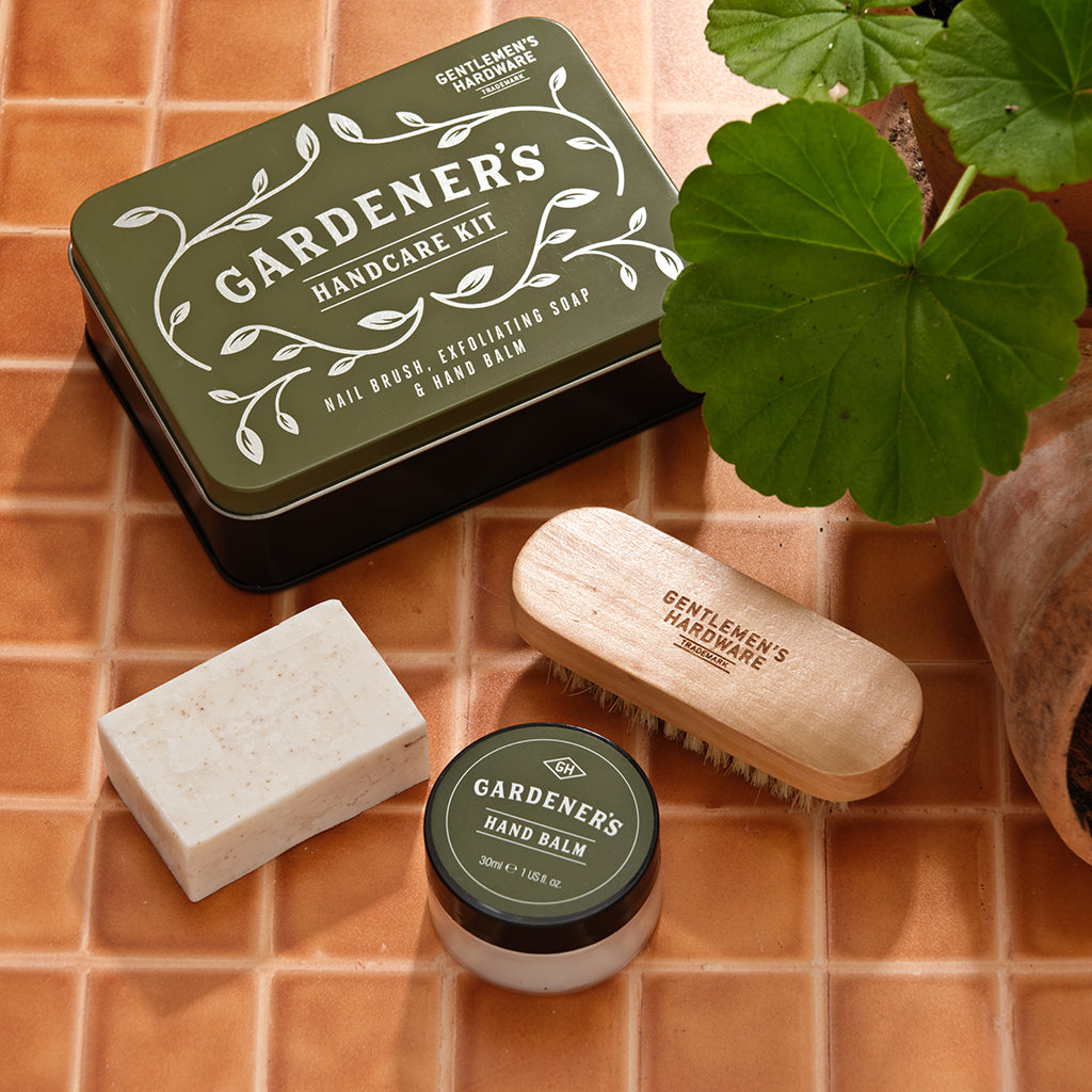 Gardener's hand care kit with tin, soap, balm, and brush on a tiled surface.