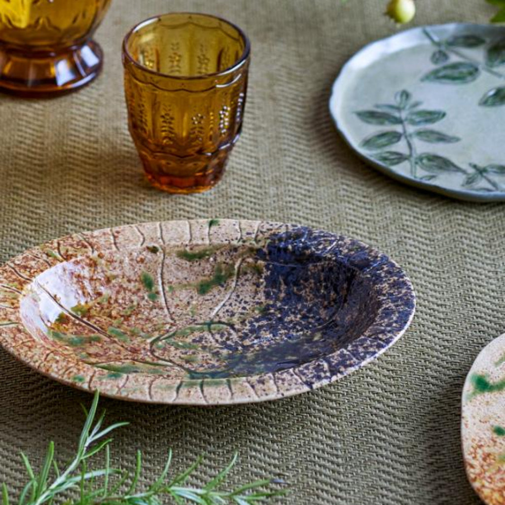 Ceramic plates and glasses with floral patterns on a textured green surface.