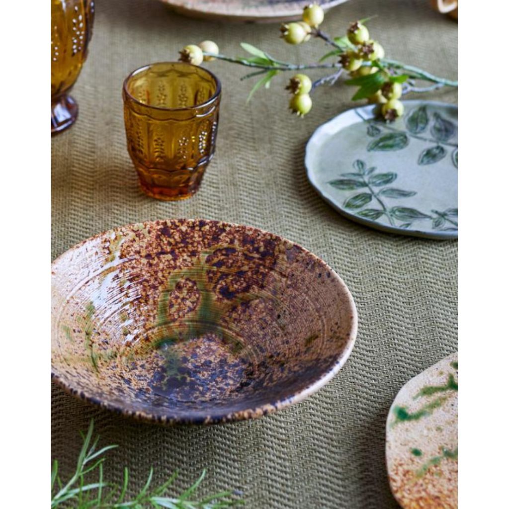 Ceramic bowl with decorative patterns on a textured surface with a glass and plate in the background.