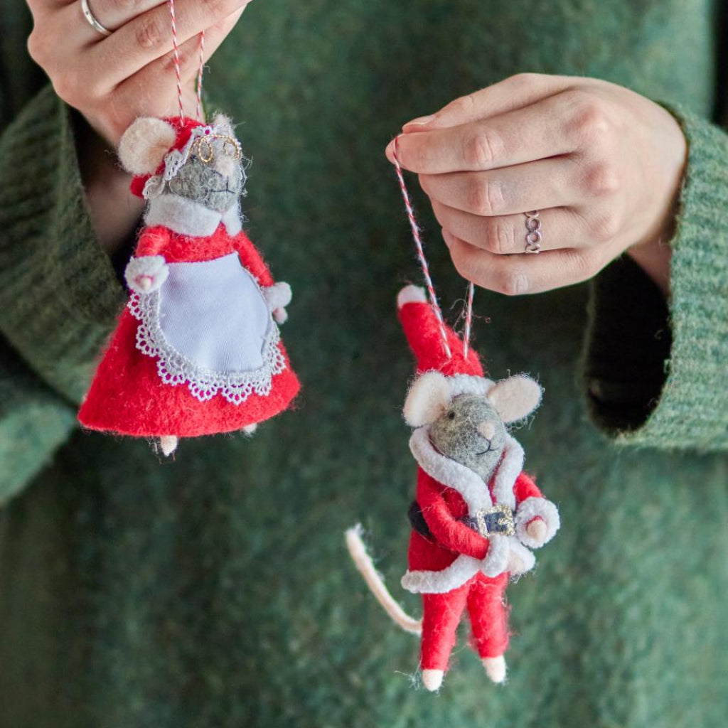 Two handmade mouse Christmas ornaments dressed as Santa Claus and a lady, held by a person against a green background.