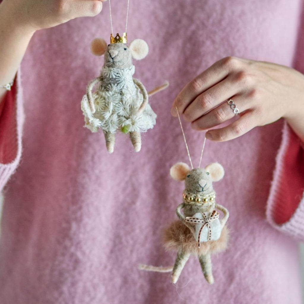 Two small mouse figurines with decorative outfits held by a person against a pink background.