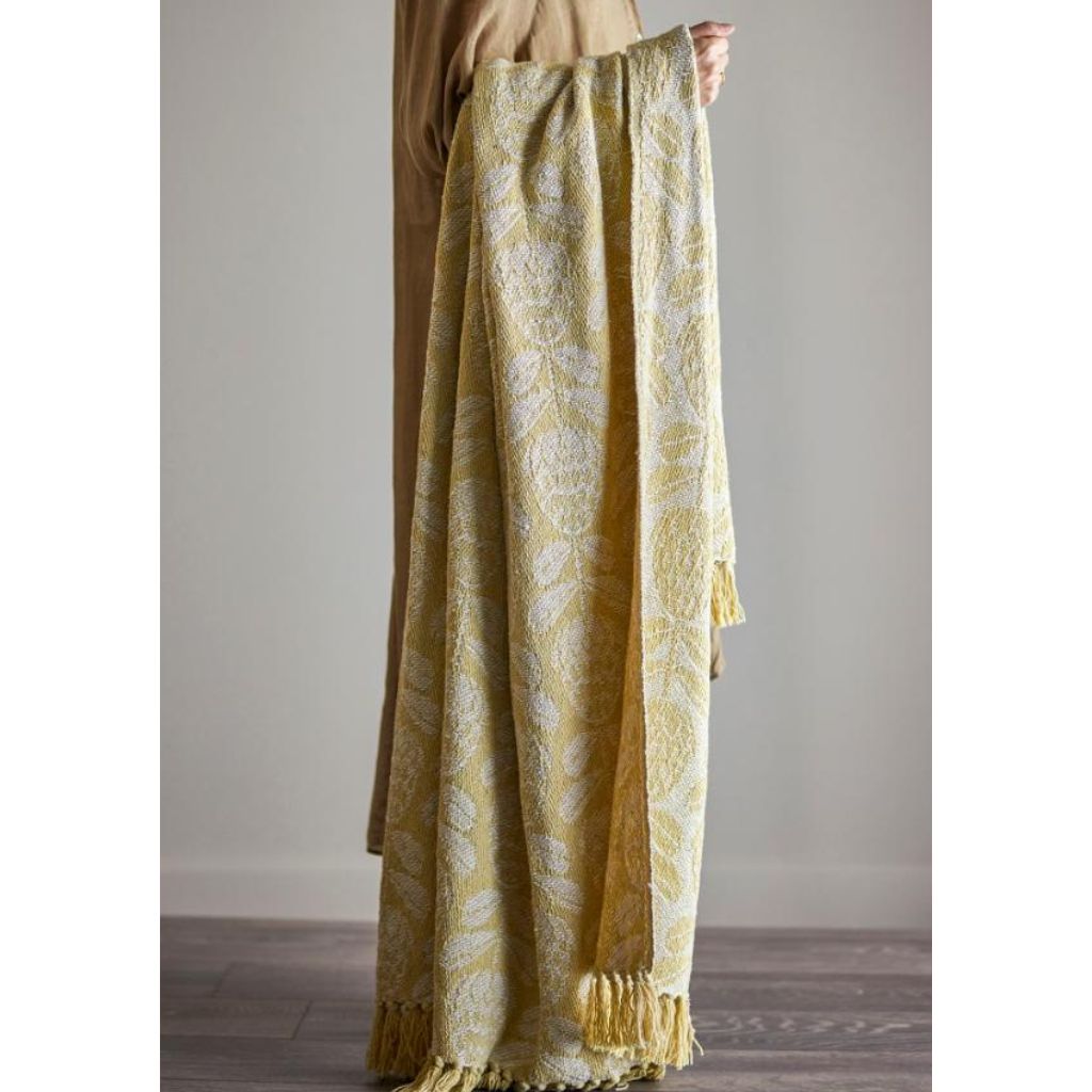 Yellow patterned throw with tassels held by a person against a neutral background