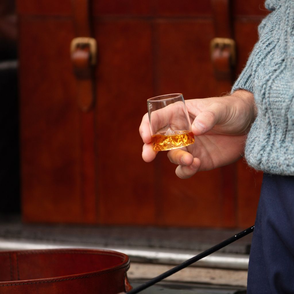 A person in a light blue cable-knit sweater holds a topographic shot glass