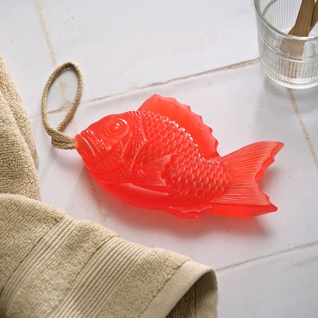 Red fish-shaped soap on a tiled surface with a towel and glass in the background