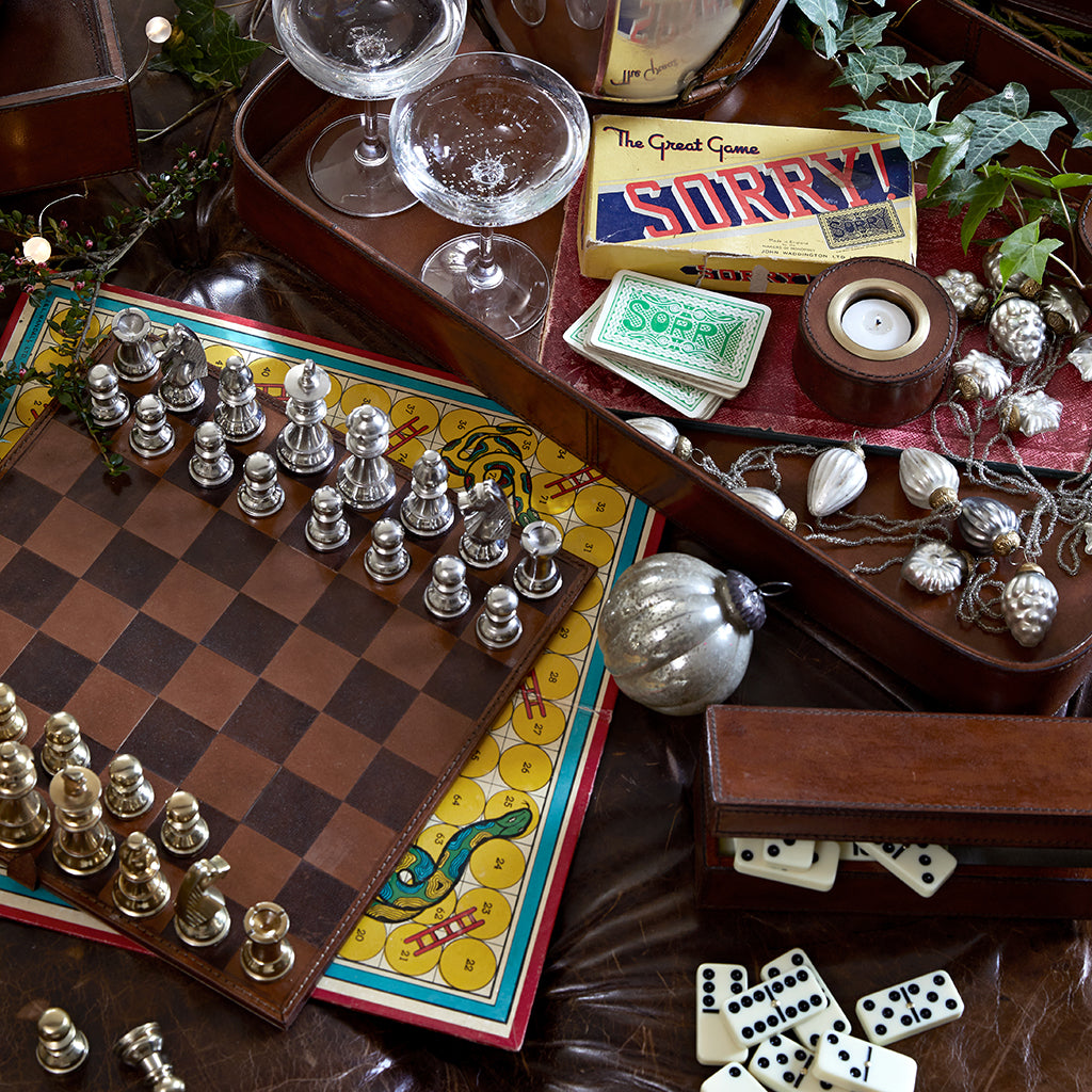 Leather chess and dominoes sets alongside a large oblong leather tray in the background with leather tealight and nickel champagne cooler