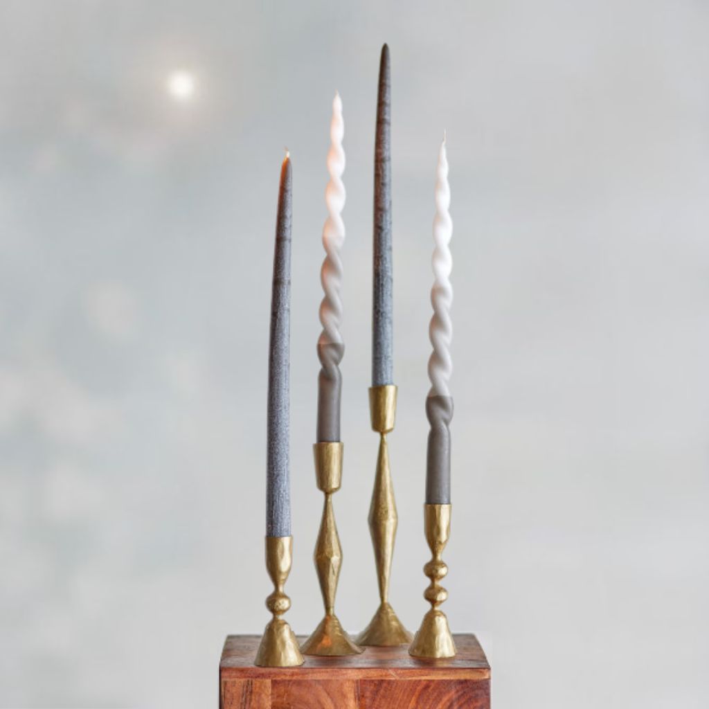 Set of tall candles in gray and gold candle holders on a wooden block with a light gray background.