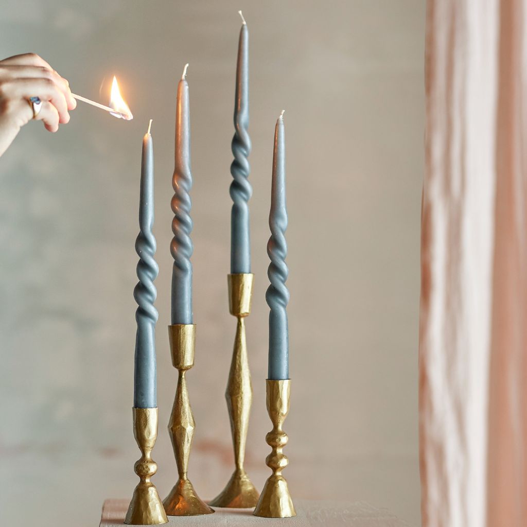 Gray twisted candles with gold holders being lit against a neutral background