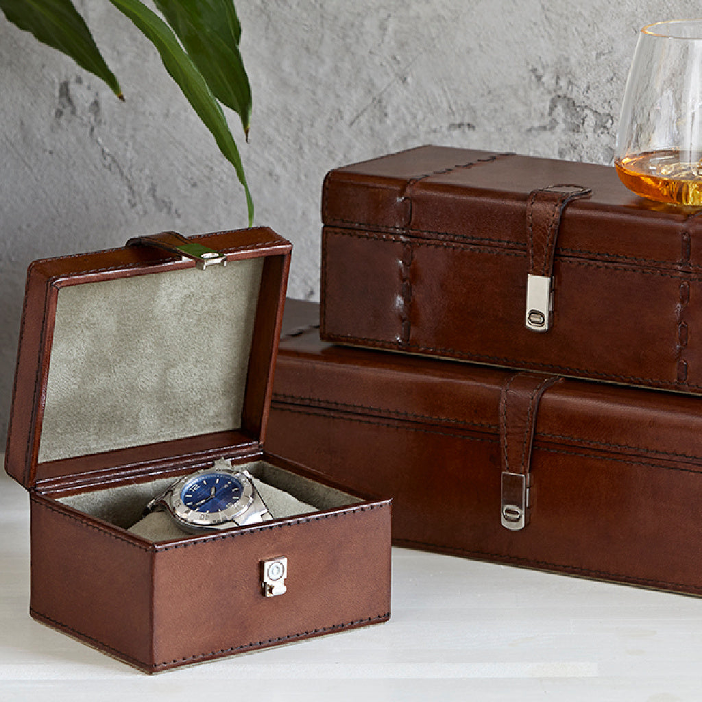 Leather stud keepsake box open with watch inside,  in front of a leather watchbox for five and Leather watchbox for three on top with a topographic glass 