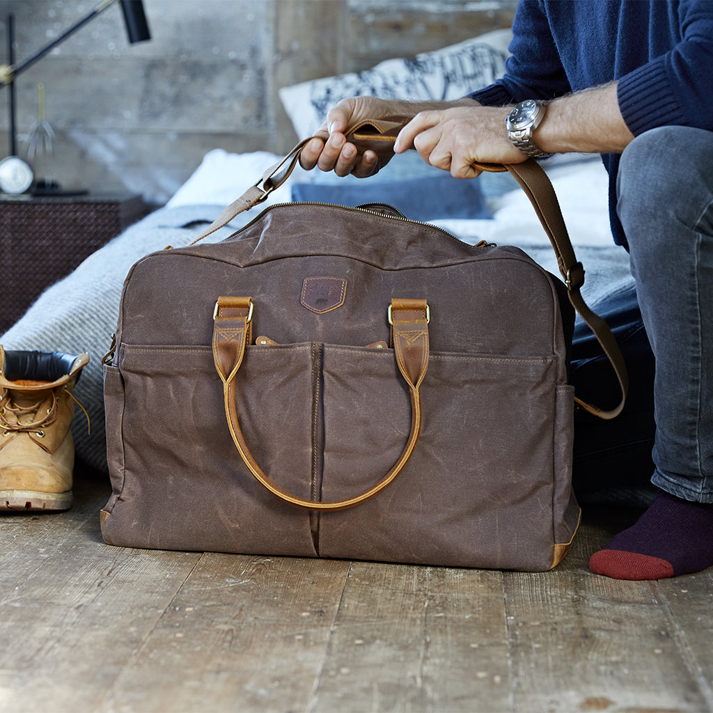 Waxed canvas weekend bacg in brown showing man holding the carry strap
