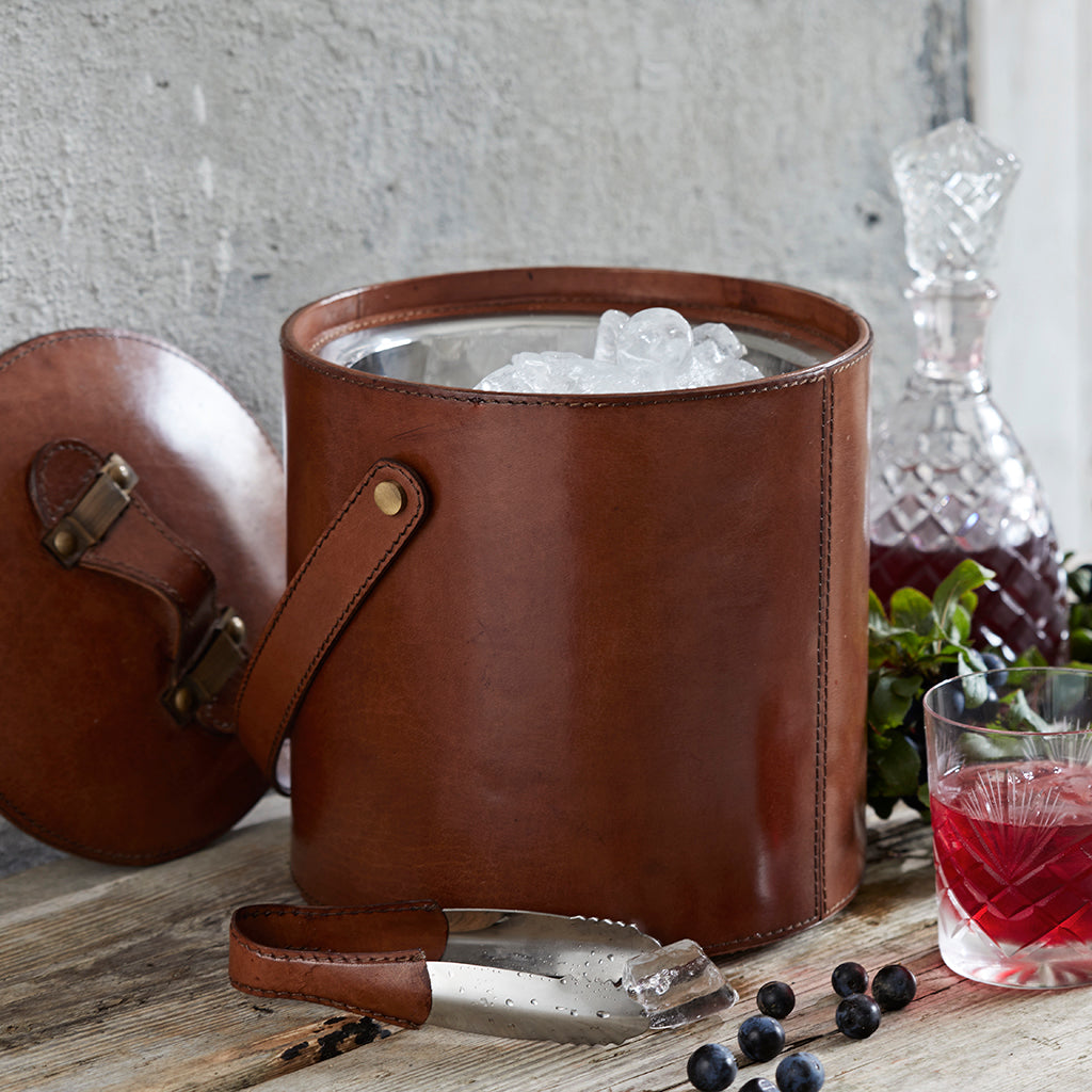 Leather ice bucket with leather handled ice tongs. shown with ice and the lid to one side