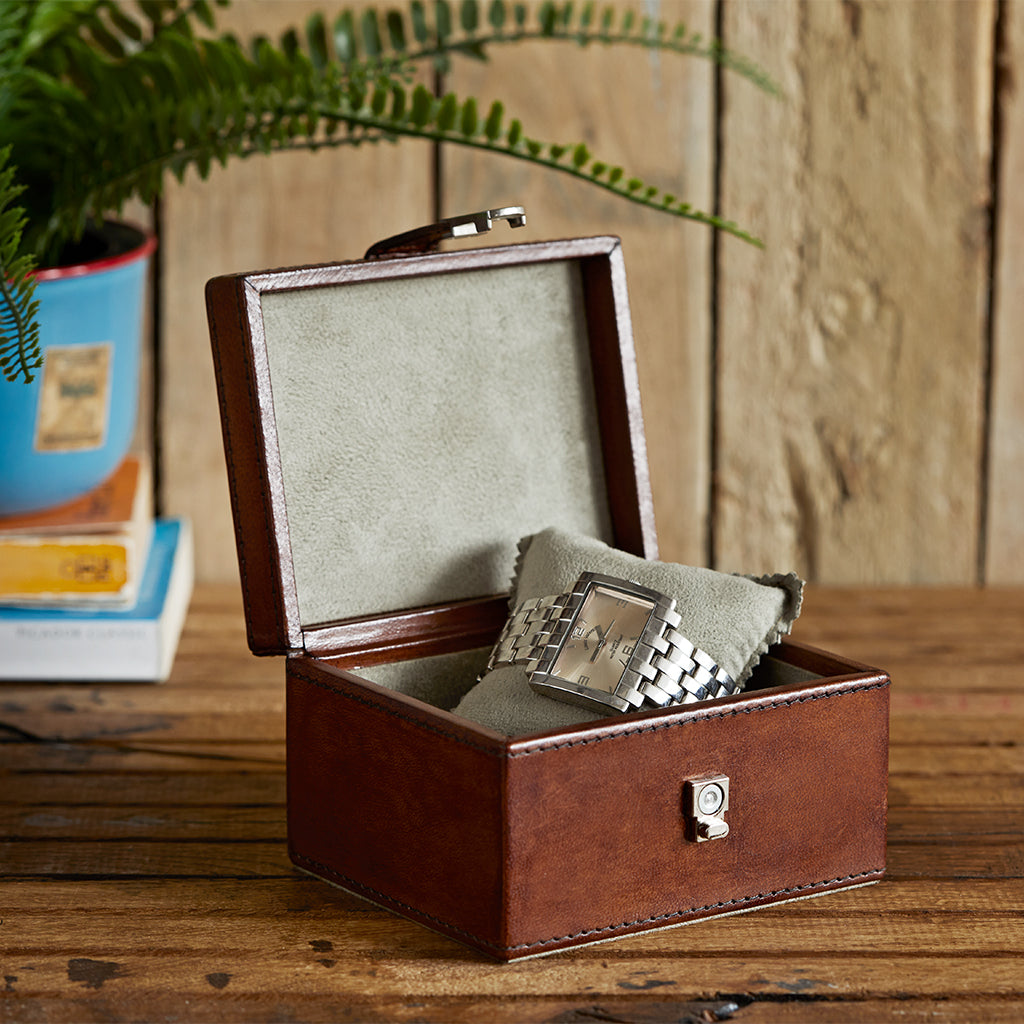 Leather stud keepsake box in conker brown open to show faux suede watch cushion with a ladies watch.