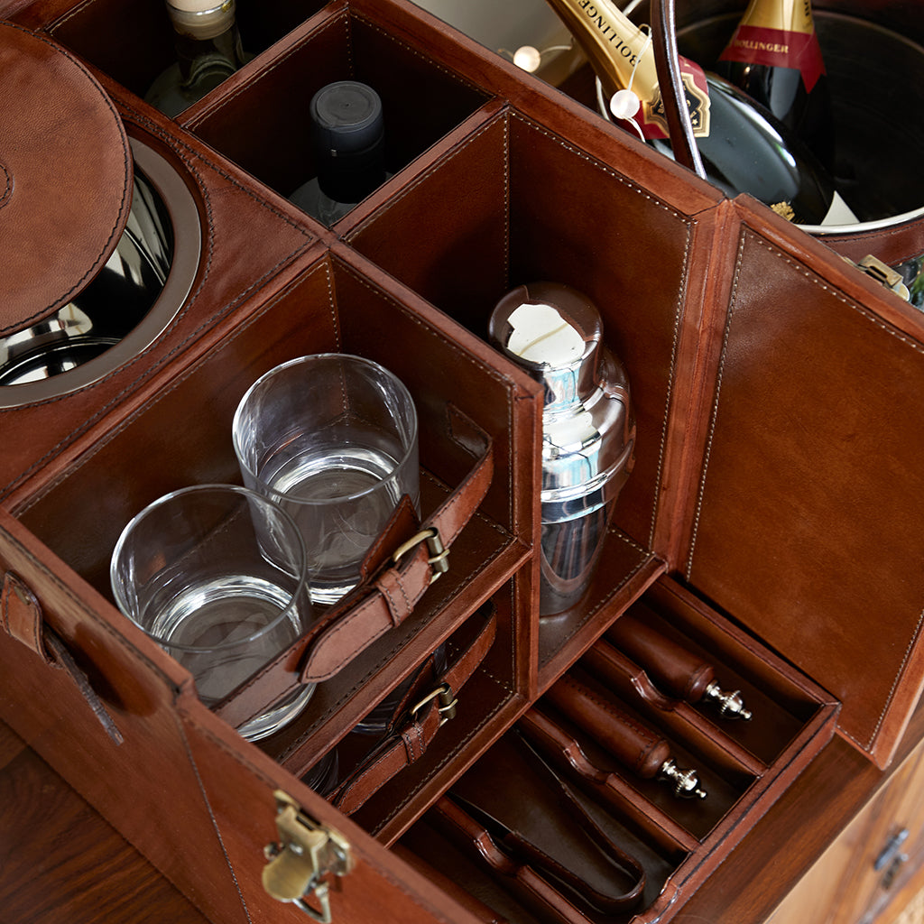 Leather mixology box open to shown the compartments, removable ice bucket and pull out drawer containing leather handled cocktail tools. With nickel champagne cooler to the side