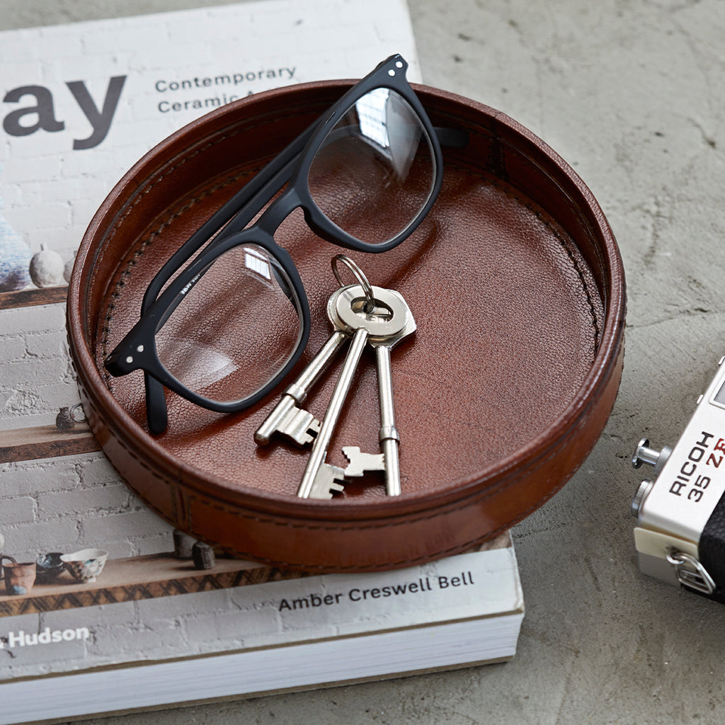 Round leather key tray for side table, shown with keys and reading glasses